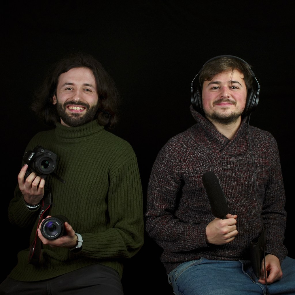 Due operatori sorridono e guardano in camera. Un tecnico del suono e un videomaker.